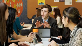 three students sitting around a table and working together