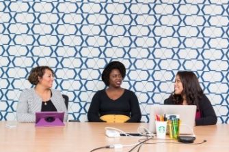 3 women sat at a table with a retro wallpaper behind