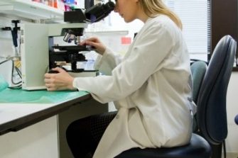 White woman in lab coat looking at a microscope