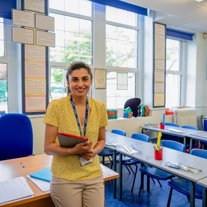 A medium closeup of a confident female teacher stood at the front of her classroom waiting for her pupils to arrive. The classroom is all ready and prepared for the new day. She is in a school in Hexham in the North East of England.