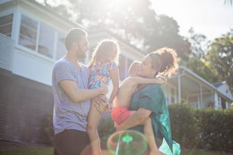 Children sit in a circle around a large piece of fabric painting homes, and rainbows and family