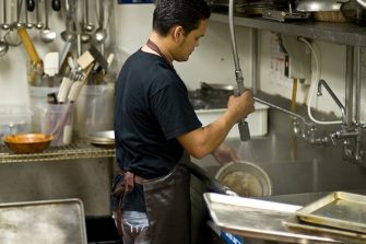 Hispanic male worker washing the dishes at a restaurant kitchen