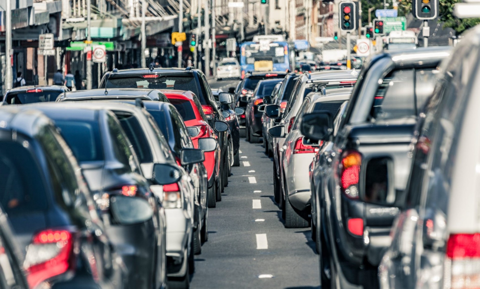 Rush hour traffic gridlock on busy Sydney main road.  Looking between two lanes of stationary vehicles with brake lights illuminated plus both red and green traffic lights.  A public transport bus is in the distance.  Horizontal, heat haze (shimmer).
