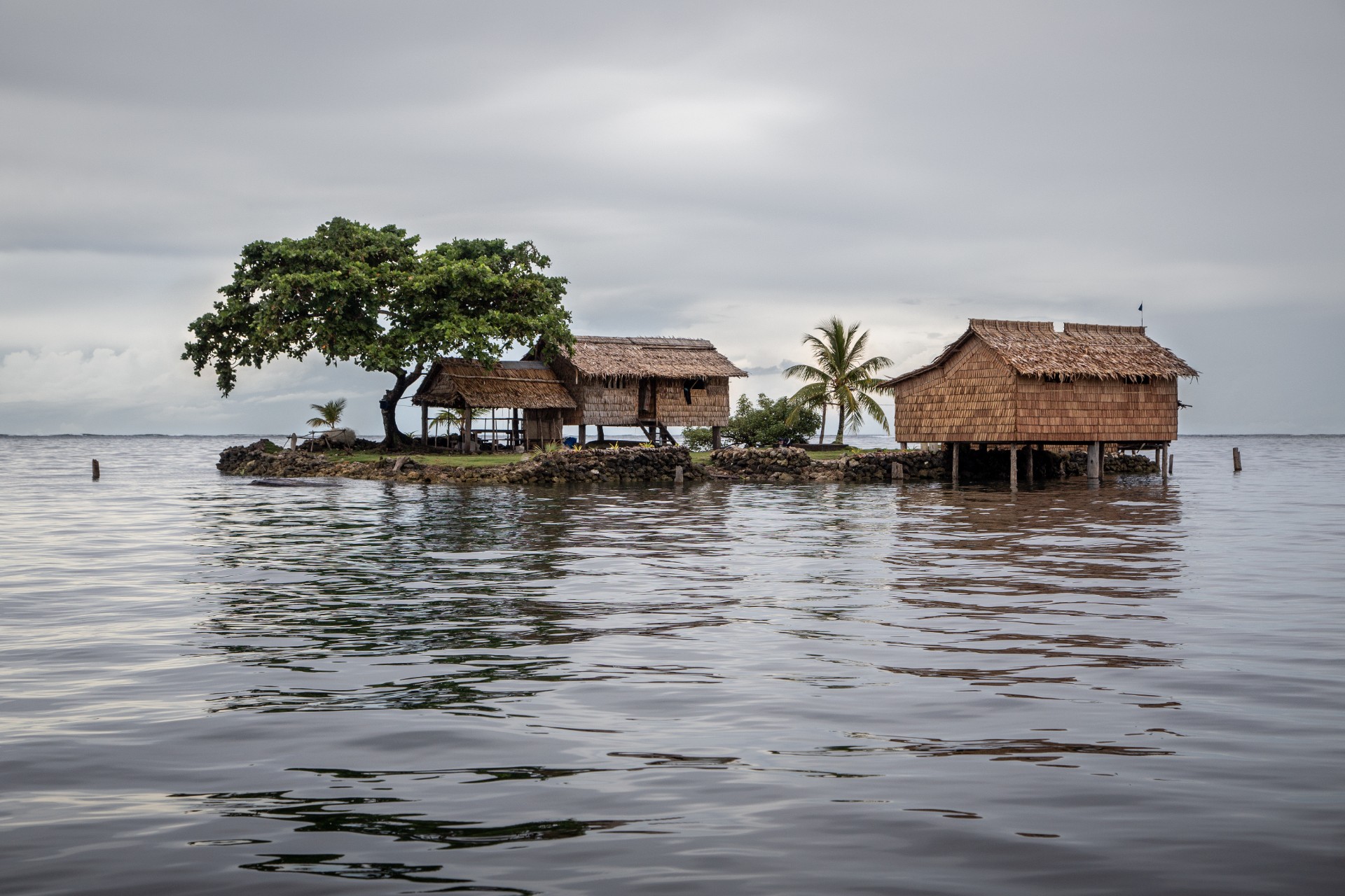 Traditional thatched houses on a small artificial island on a gloomy day in Lau Lagoon, off the island of Malaita in the Solomon Islands.