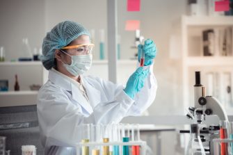Masked scientist hold test tubes holding red liquid in a laboratory 