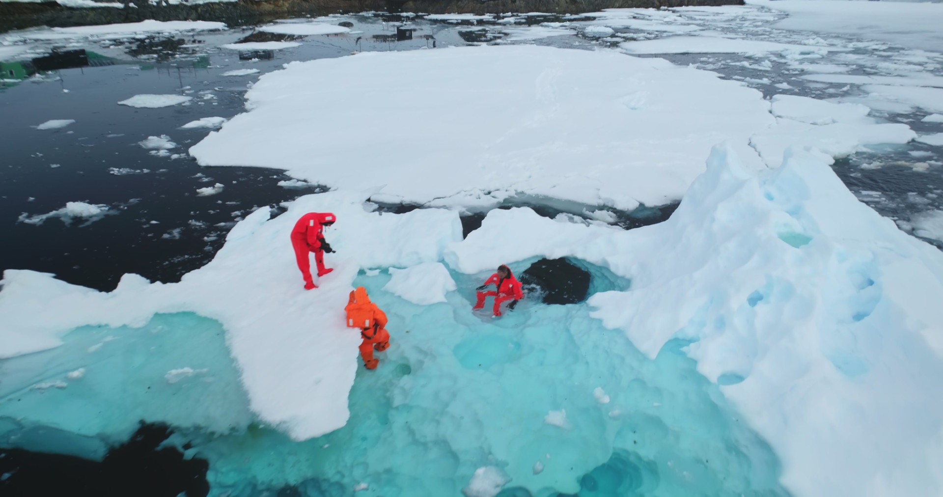 Science exploration on South Pole. People explore global warming in Antarctica. Group of scientists in orange wetsuits take samples and measure melting glacier water, climate change problem. Aerial
