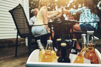 Group, people and drinks at barbecue in backyard, summer and vacation for holiday, celebration or event. Friends, cheerful and bbq with cooler box for dinner, party or reunion with alcohol in America.