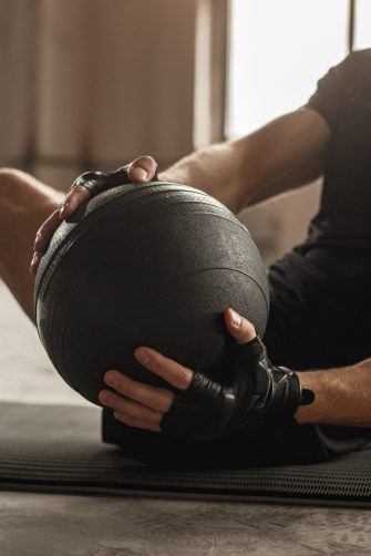 Side view of crop unrecognizable athletic male doing side twist exercise with medicine ball during intense functional training in gym