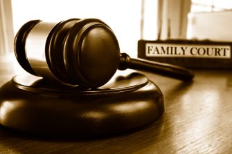 Close up of wooden figurines of family with child and gavel on background of judge conducting divorce process. Concept of alimony, family law and child custody.