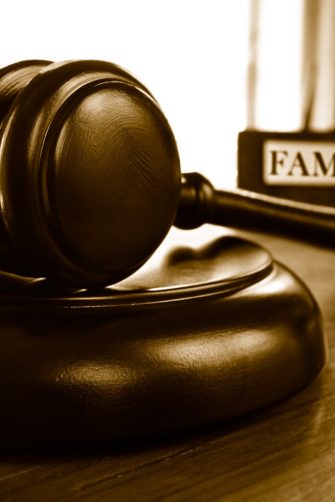 Close up of wooden figurines of family with child and gavel on background of judge conducting divorce process. Concept of alimony, family law and child custody.