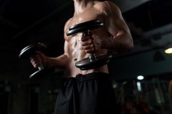 close up of young man with dumbbells flexing muscles in gym
