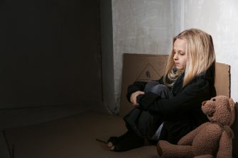 Homeless little girl sitting on floor near wall