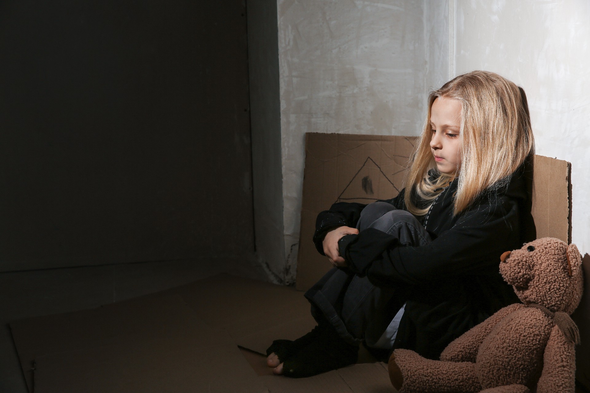 Homeless little girl sitting on floor near wall
