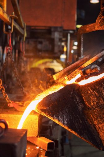 Foundry bucket pouring hot molten metal into casting mold. Mettalurgy and steel production.