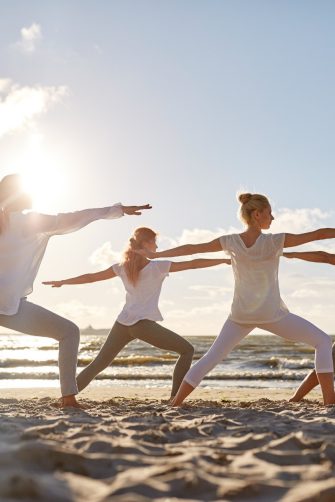 fitness, sport, yoga and healthy lifestyle concept - group of people making warrior pose on beach