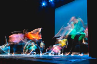 Group of dancers in coloured clothes dancing on the stage in long exposure