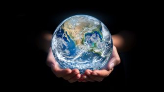 A photo illustration of the planet Earth held gently in human hands