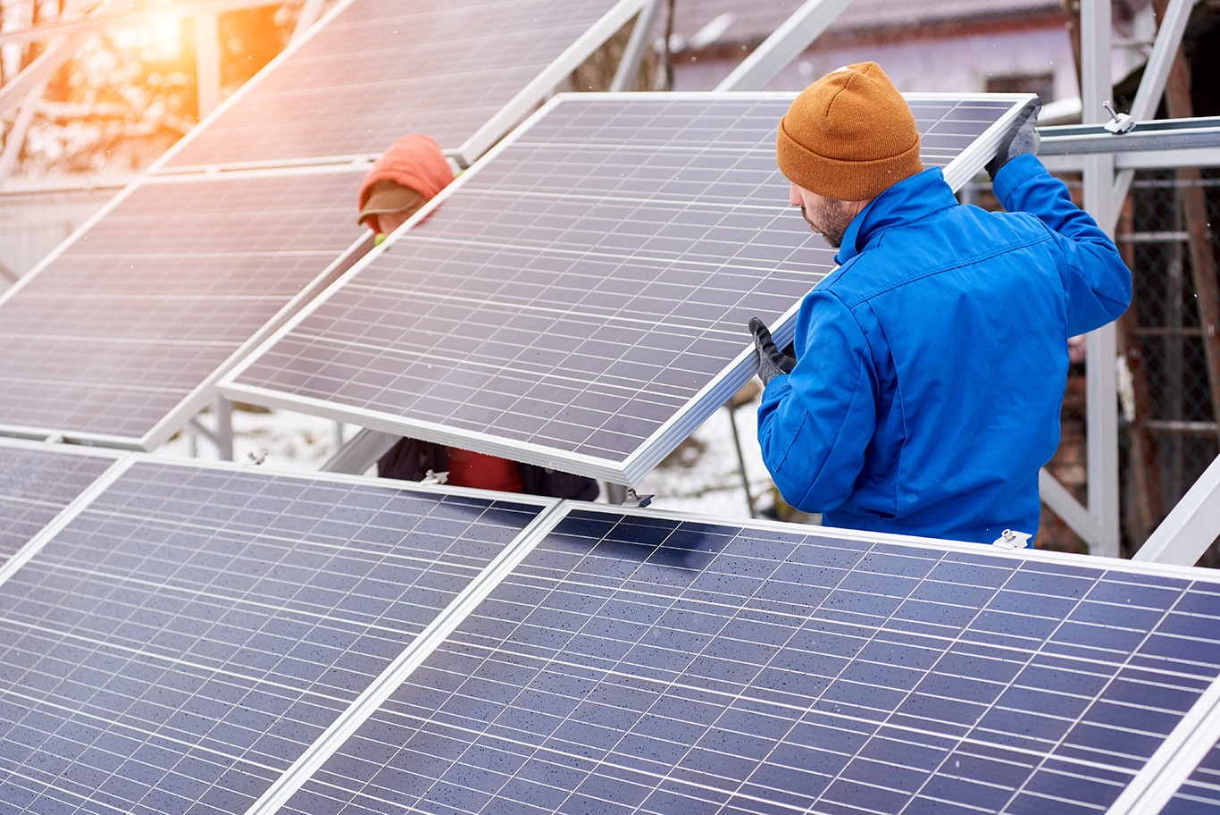 Technicians in blue suits mounting photovoltaic solar panels on roof of modern house. Solar modules as ecological renewable energy sources. Alternative production modules power sustainable resources