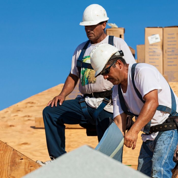 Roofers laying underlayment on a home that is under construction.