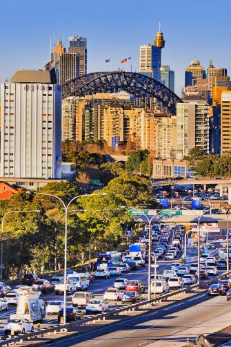 Rush hour traffic gridlock on busy Sydney main road.  Looking between two lanes of stationary vehicles with brake lights illuminated plus both red and green traffic lights.  A public transport bus is in the distance.  Horizontal, heat haze (shimmer).