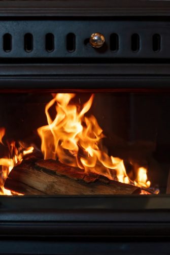 Wood stove fireplace and burning firewood behind glass door, Black metal fireside, fire flame radiate heat, warm home interior,