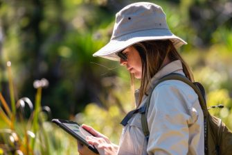 A woman wearing a hat is focusing on a tablet, likely collecting wildlife data for a citizen science project