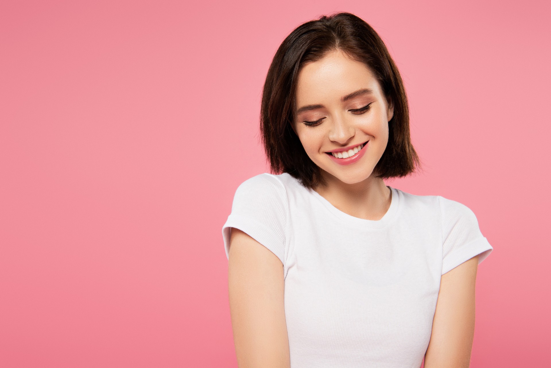 beautiful smiling shy girl looking down isolated on pink