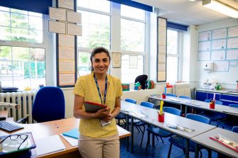 A medium closeup of a confident female teacher stood at the front of her classroom waiting for her pupils to arrive. 