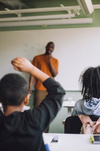 A medium closeup of a confident female teacher stood at the front of her classroom waiting for her pupils to arrive. 