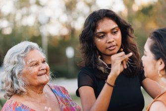 Three Generations Of Aboriginal Australian Women Doing Traditional Ochre Face Painting