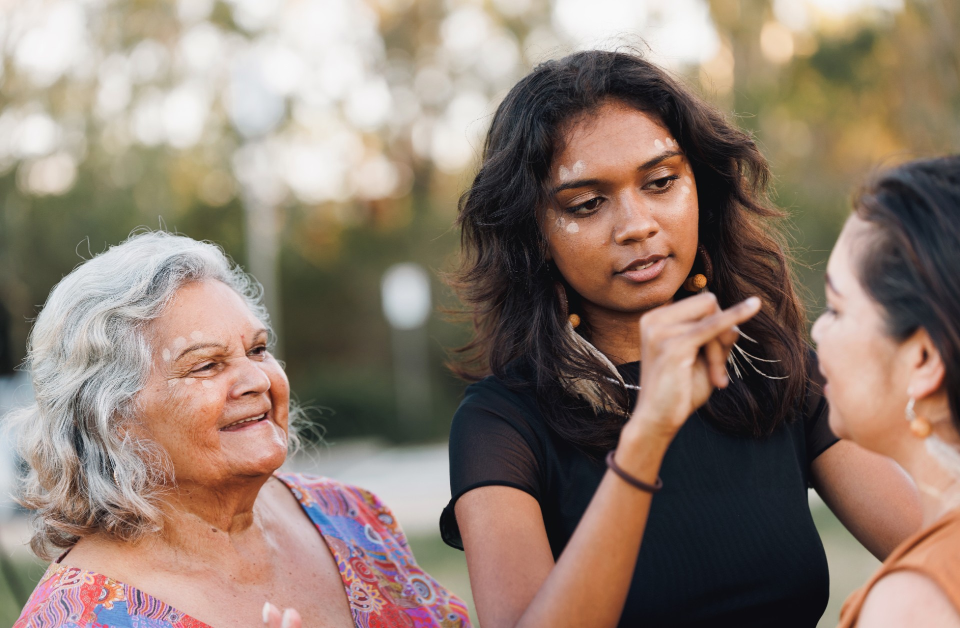 Three Generations Of Aboriginal Australian Women Doing Traditional Ochre Face Painting