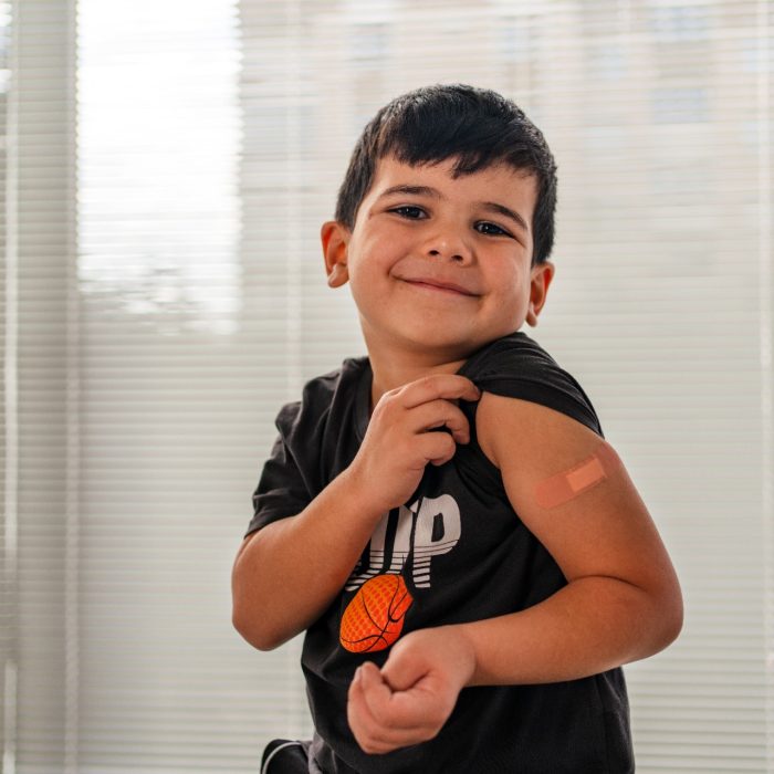 Vaccinated young boy smiling while showing bandaid on arm after a needle
