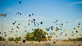 High school students toss their mortar boards into air to celebrate their graduation.