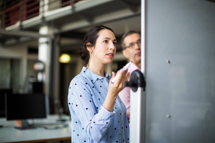Businesswoman standing with colleague while looking at whiteboard during meeting in creative office