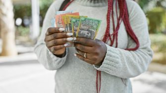 Australian currency held by a woman with braids outdoors in a lush park.