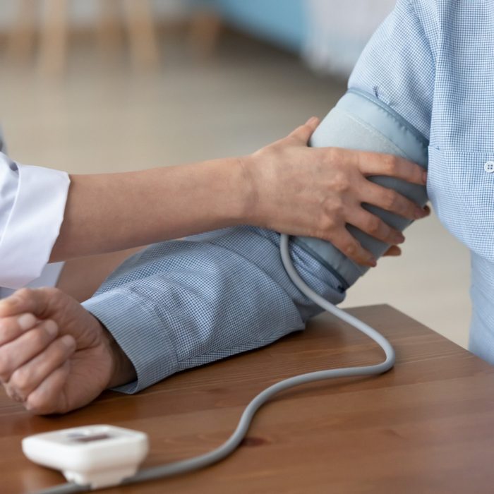 Crop close up caring female nurse check examine elderly male patient at consultation in hospital or clinic. Woman doctor measure high low blood pressure or heart rate with pulsometer monitor.