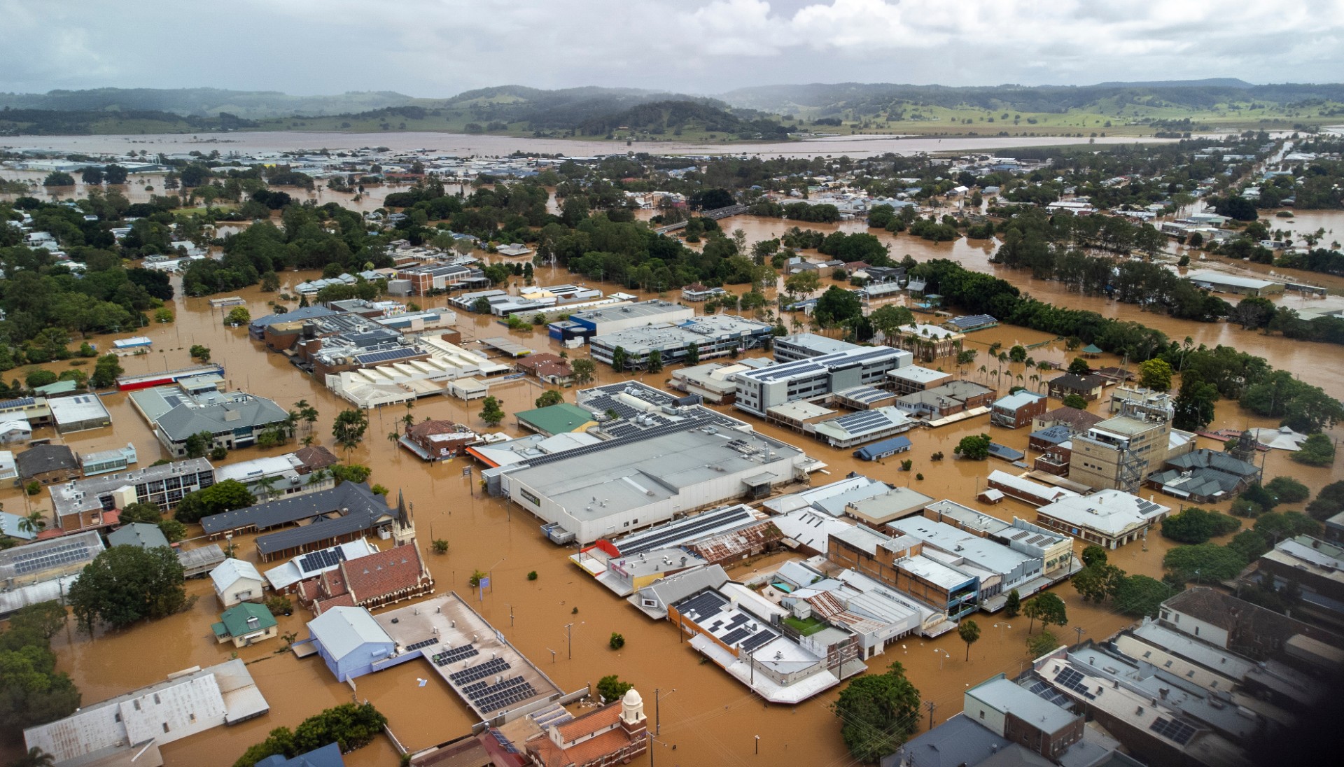 Brown floodwaters fill the streets of Lismore, submerging cars and flooding businesses