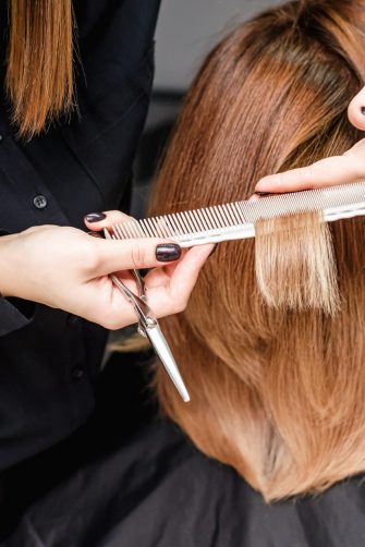 Hairdresser is cutting woman hair in hair salon, close up, rear view.