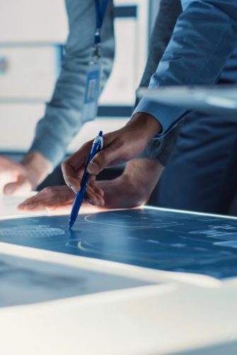 Engineer, Scientists and Developers Gathered Around Illuminated Conference Table in Technology Research Center, Talking, Finding Solution and Analysing Industrial Engine Design. Close-up Hands Shot