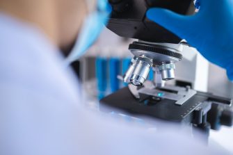Scientist analyzing microscope slide at laboratory. Young woman technician is examining a histological sample, a biopsy in the laboratory of cancer research