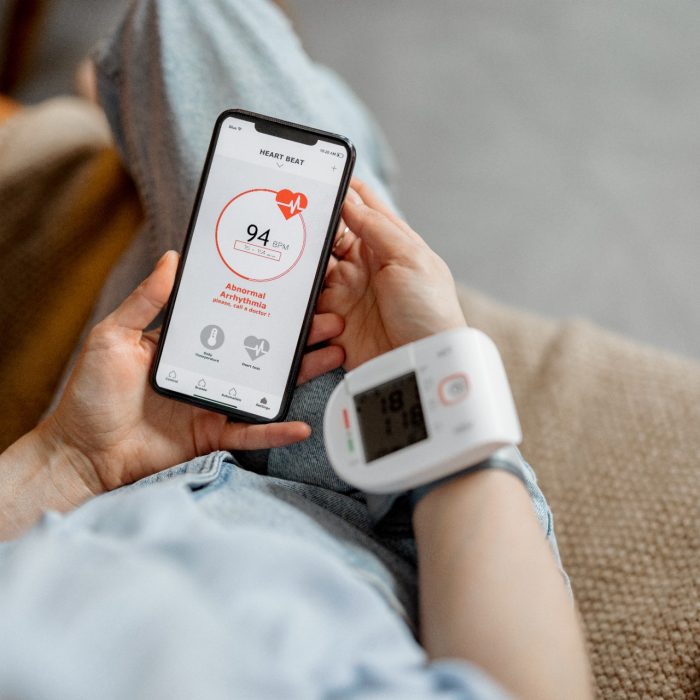 Woman measure heart rate and pressure with smart technology in phone while sitting on sofa at home. Health and wellness concept. 
