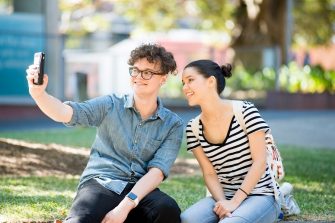 Students smile for a selfie while sitting on the lawn