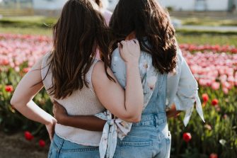 Two young women hold each other while looking into field of red tulips
