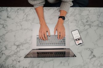 Photo of person typing from above, laptop and phone in view