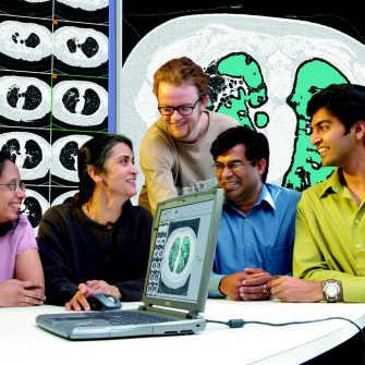 A group of people sitting around a laptop