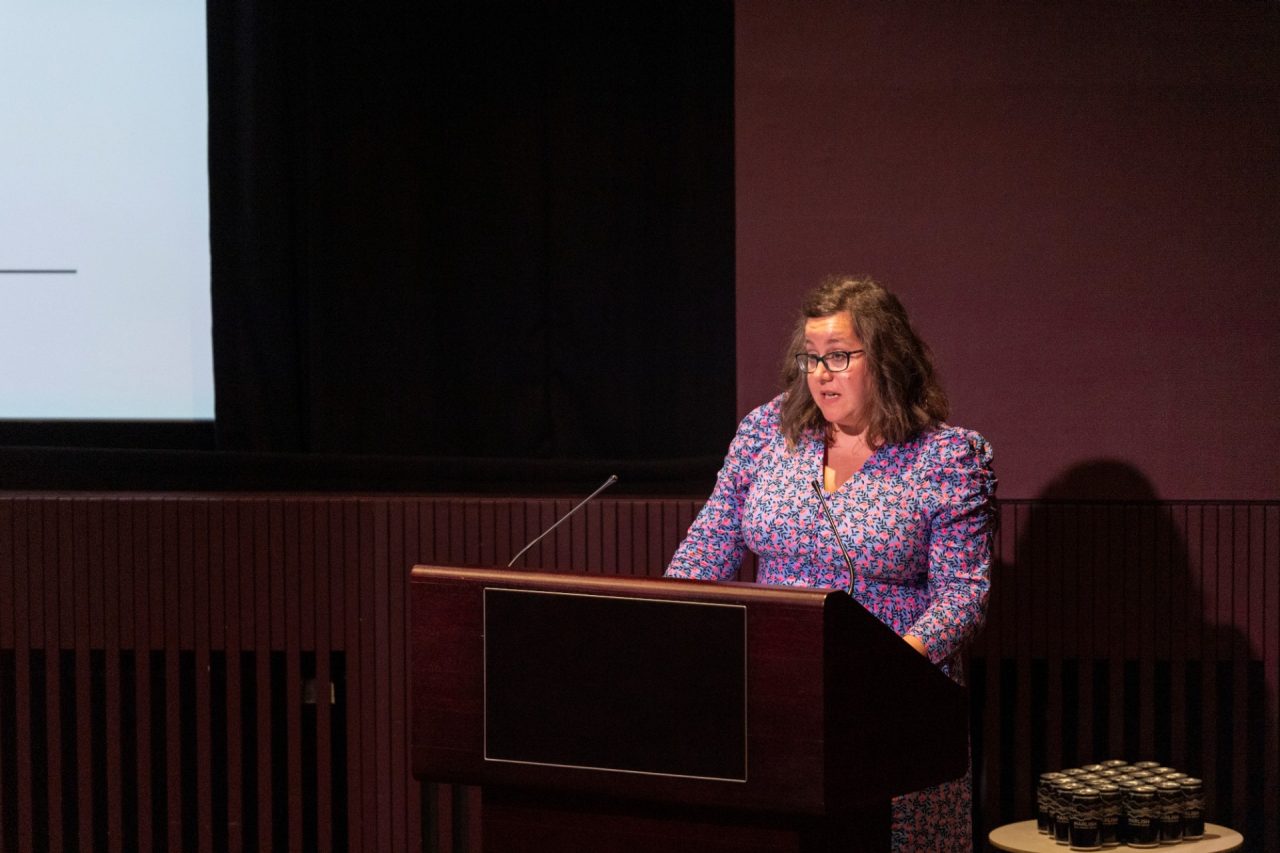 A person in a purple and pink dress speaks at a lectern
