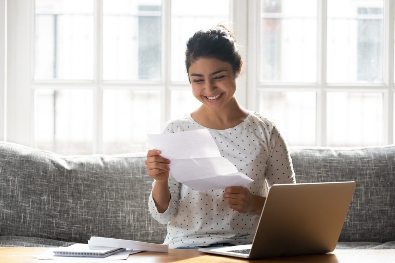 Woman sitting on couch at home reading paper notice receive good news feels happy, cheerful student female looking at document enjoy exam results or college admission letter concept