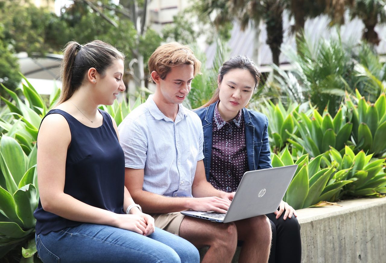 Three students sitting on a wall, working