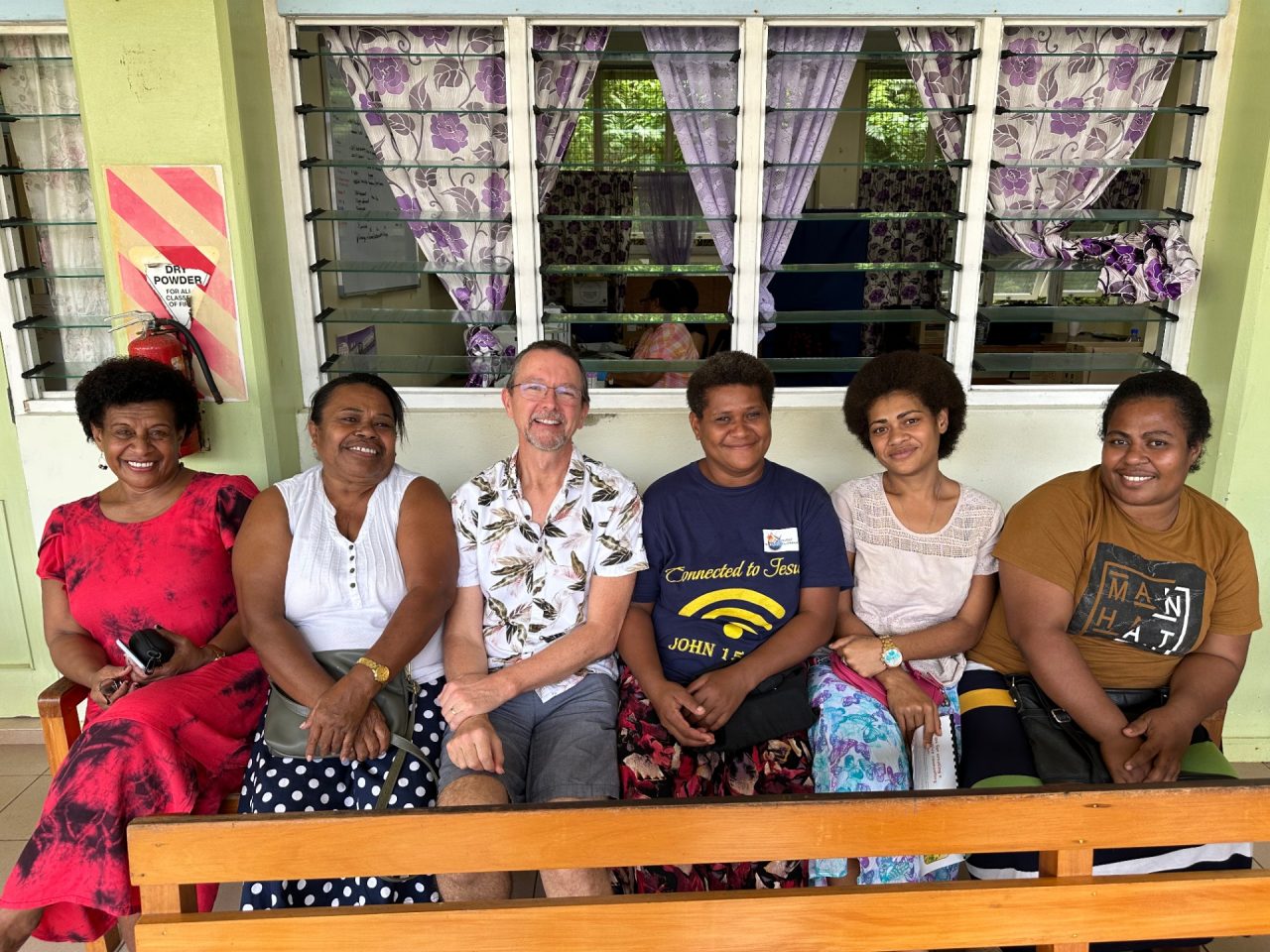 A man sitting with five women outside a building.