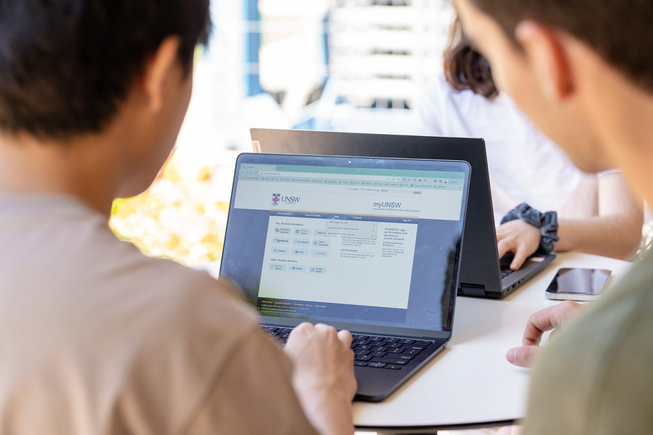 Two students using a laptop at a table beside Library Lawn